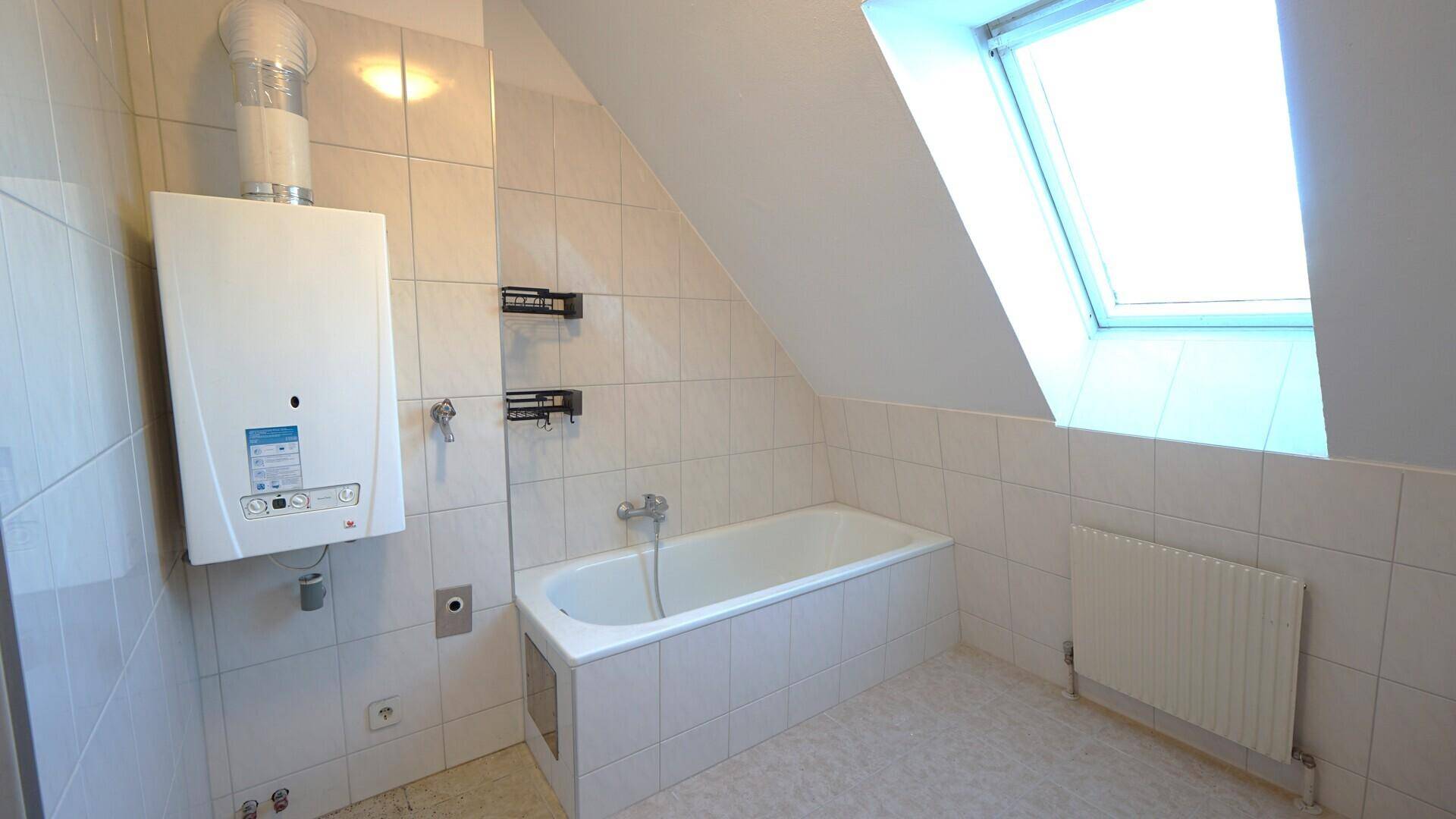 Badezimmer im Dachgeschoss mit Badewanne, Gastherme und weißen Wandfliesen.