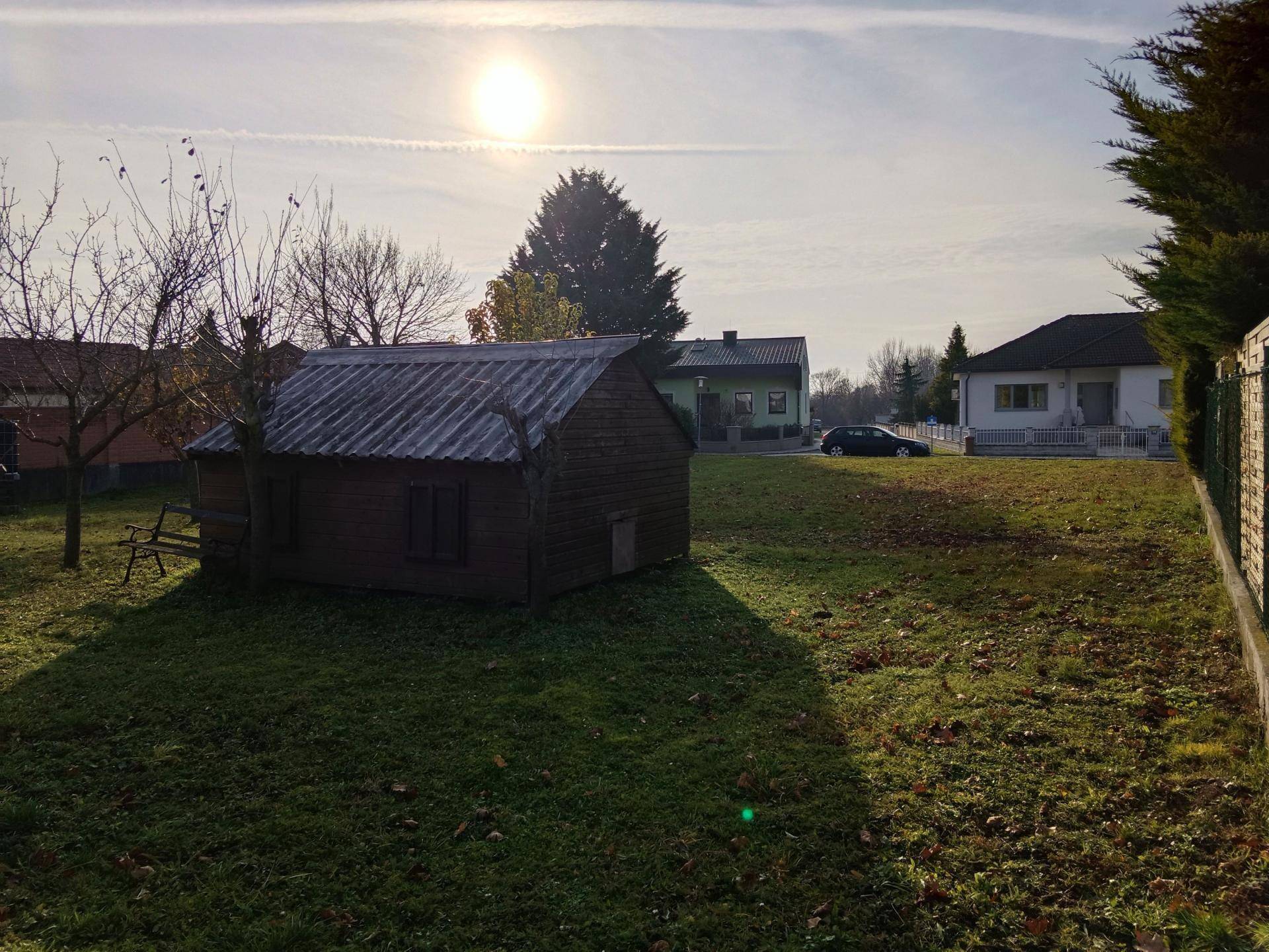 Winterlicher Gartenbereich mit einer Holzhütte und kahlen Bäumen unter einem sonnigen Himmel.