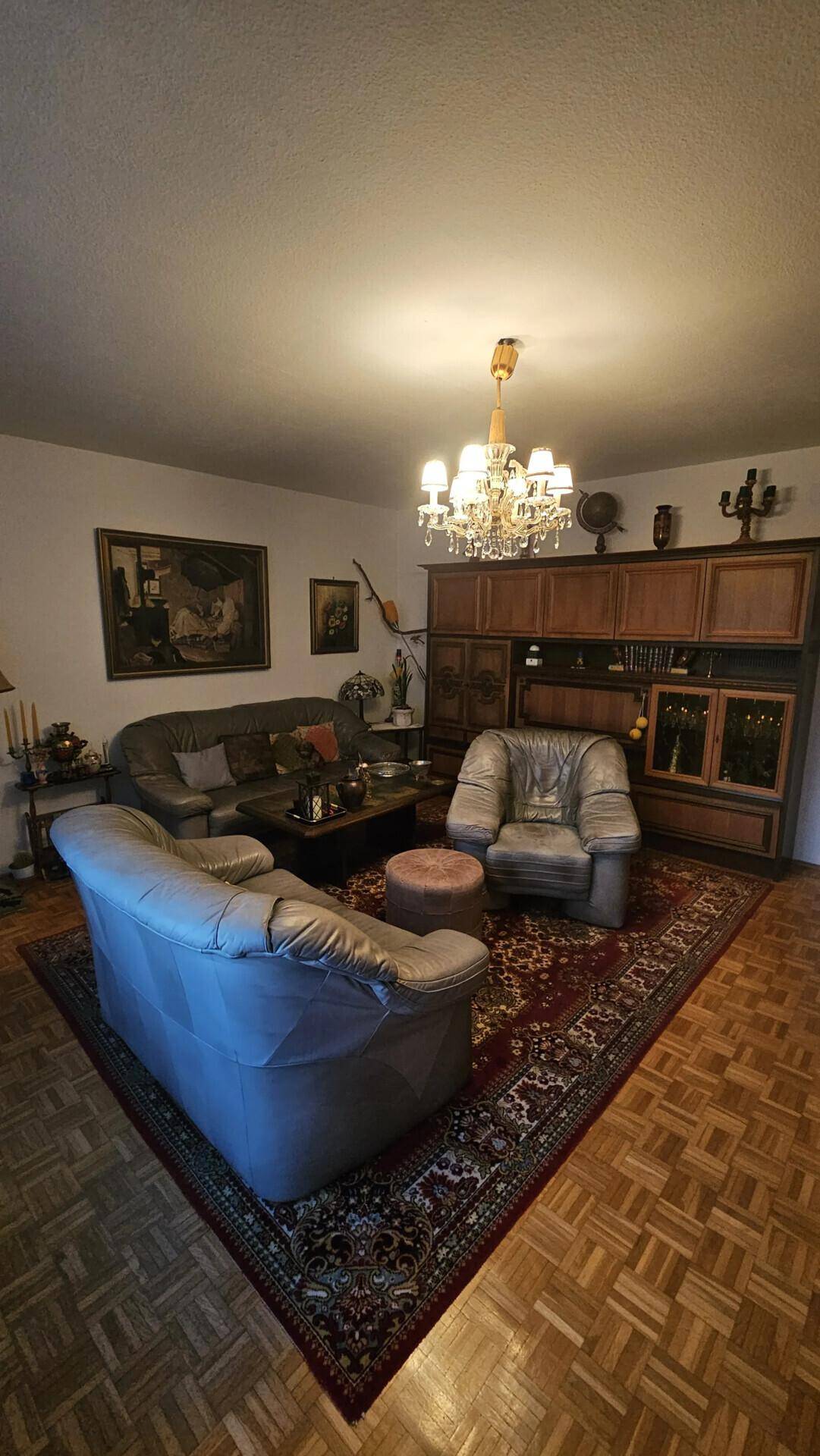 Geräumiges Wohnzimmer mit Parkettboden, bequemen Ledersofas und einem großen Orientteppich.