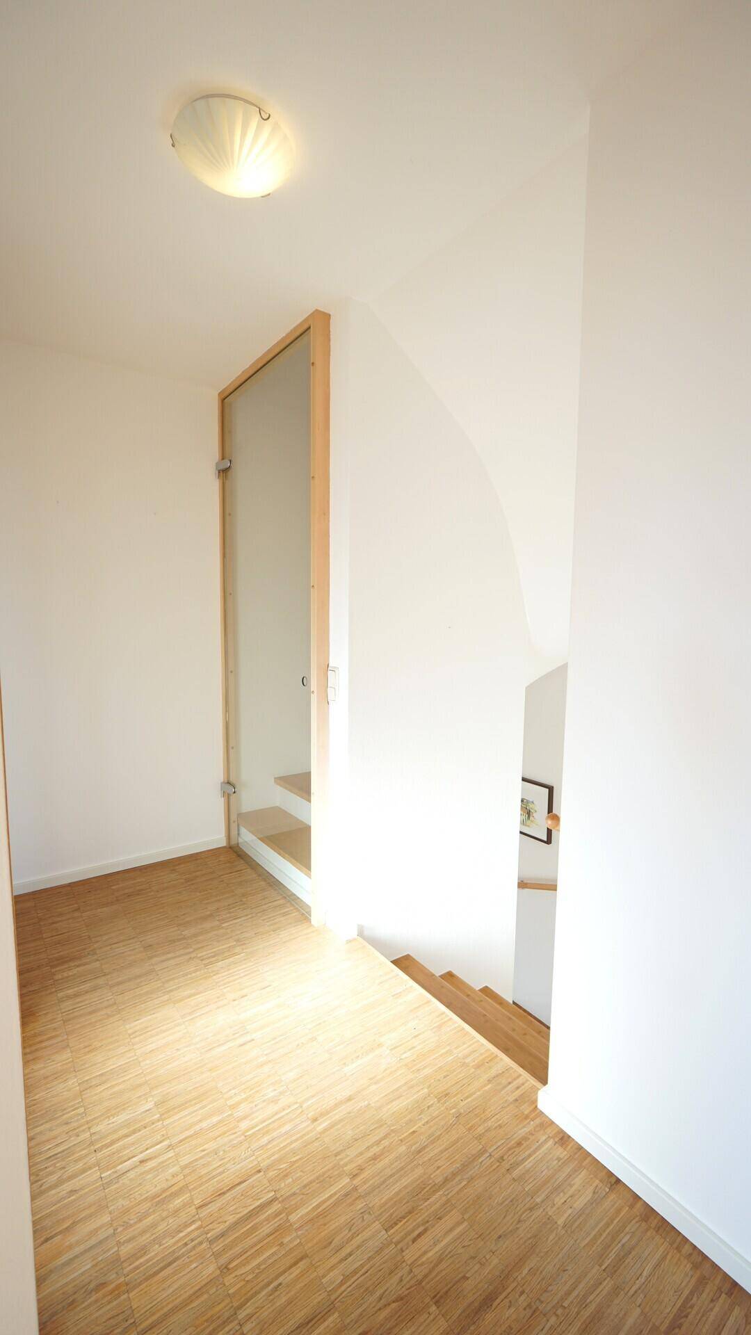 Heller Flur im Obergeschoss mit Holzparkett und einer modernen Glastür zum Treppenhaus.