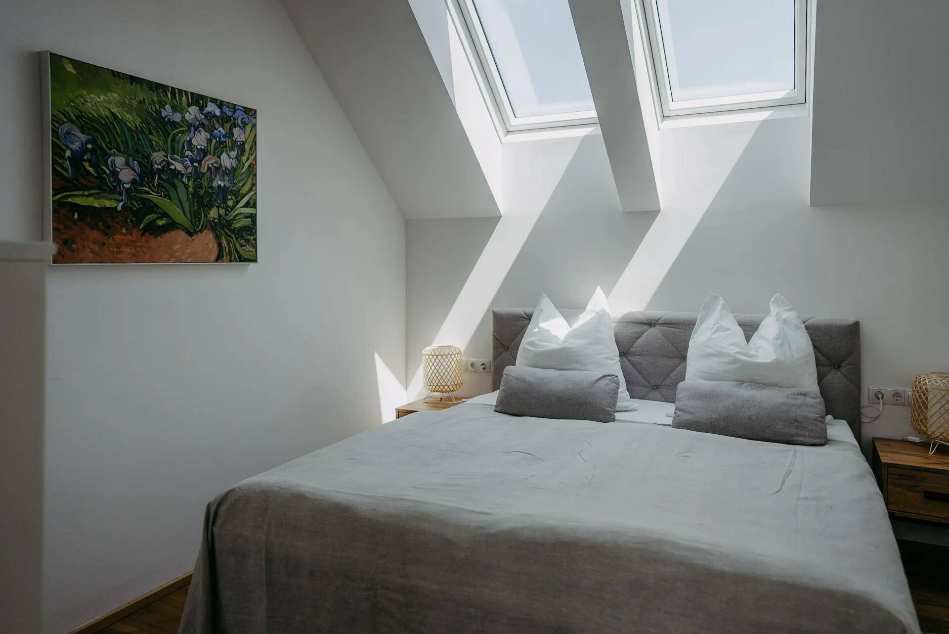Helles Schlafzimmer mit Dachschrägen, großen Dachfenstern und modernem Doppelbett.
