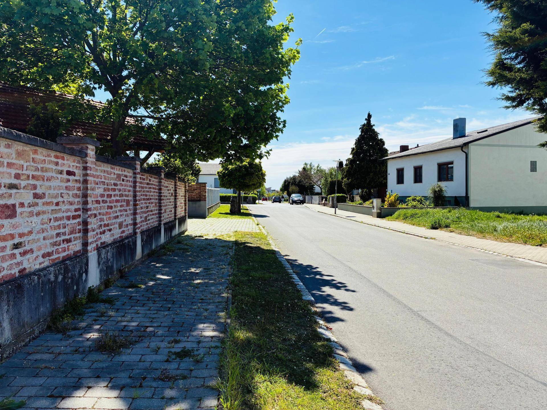 Wohnstraße mit altem Baumbestand und einer markanten Ziegelmauer, die das Grundstück begrenzt.