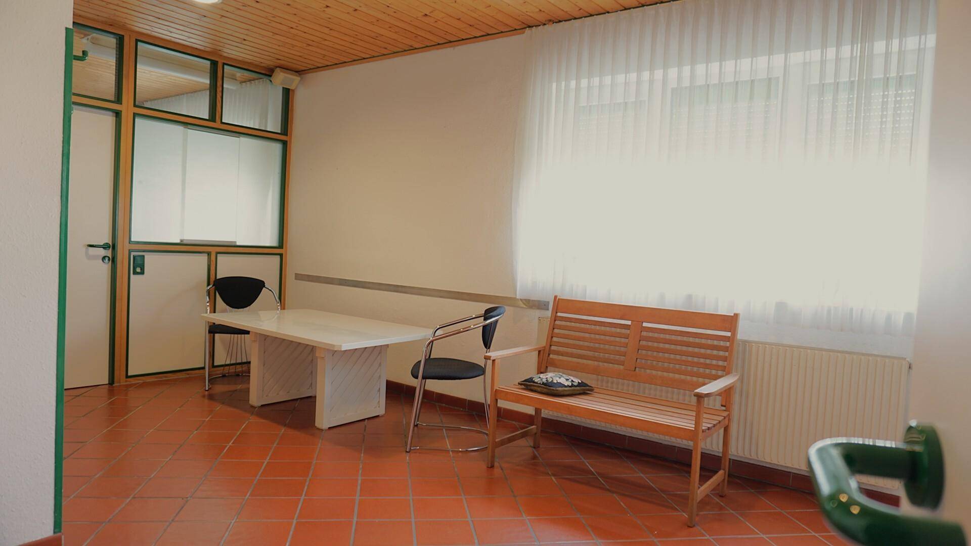 Vielseitiger Raum mit Fliesenboden, Holzbank und großem Fenster.
