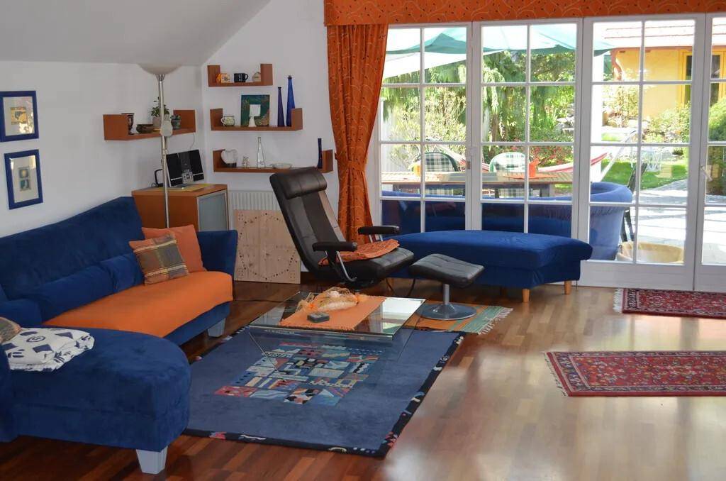 Helles Wohnzimmer mit blauen Sofas, Holzboden und großen Fenstern zum Garten.