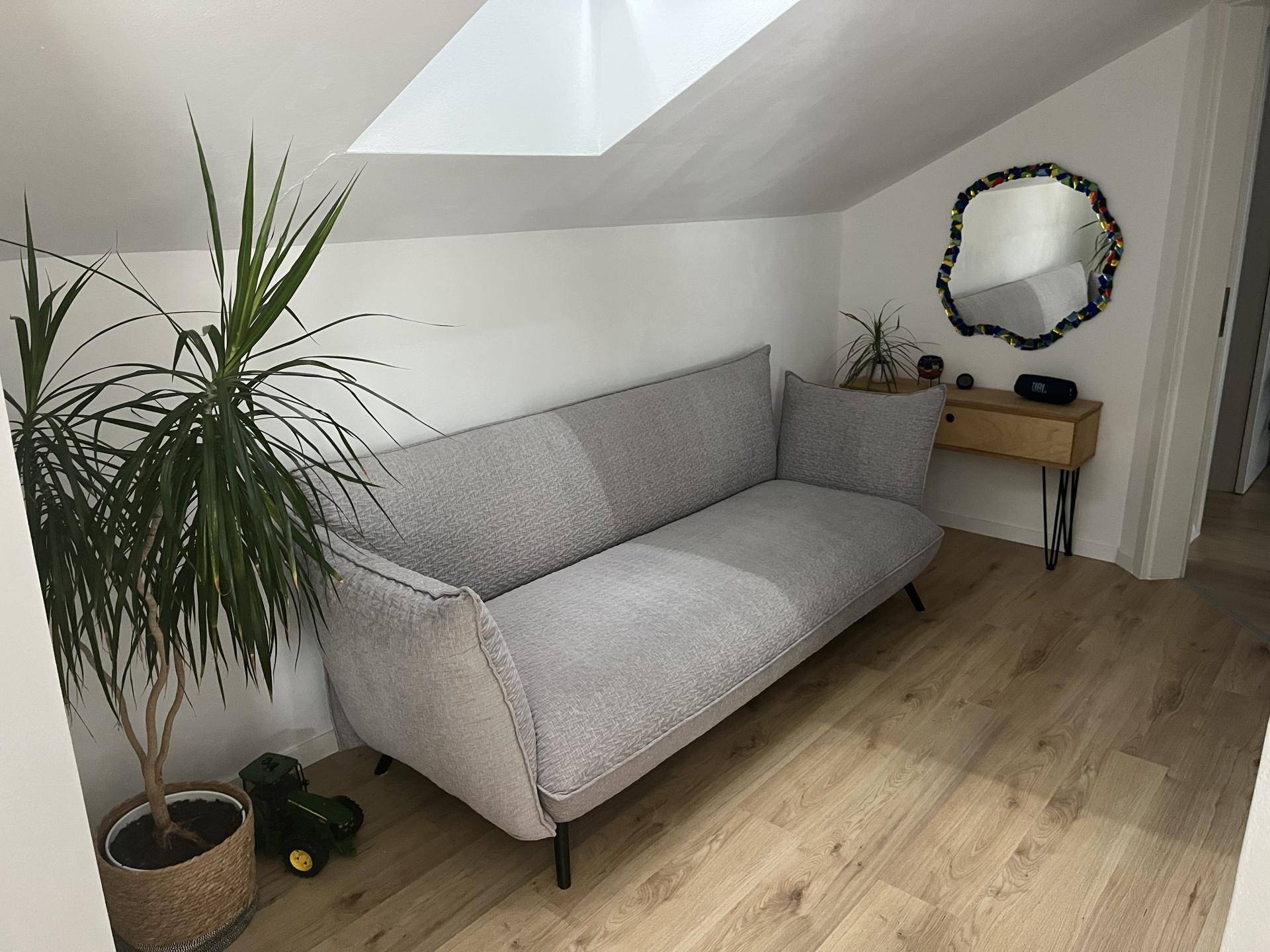 Gemütliches Wohnzimmer im Dachgeschoss mit Schrägdach und modernem Sofa.