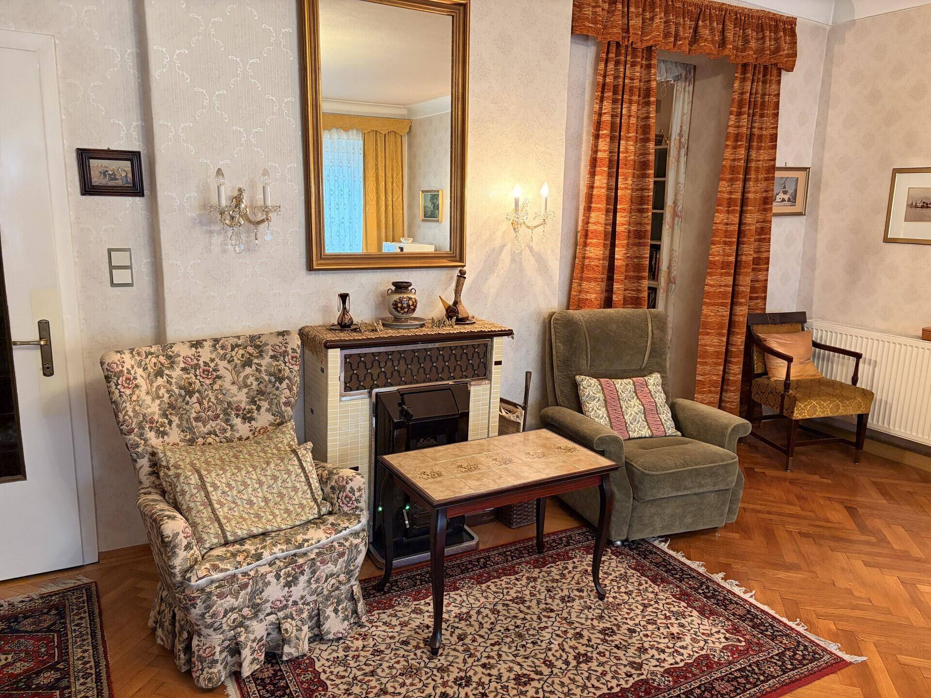 Gemütliche Sitzecke im Wohnzimmer mit traditionellem Kachelofen und klassischen Sesseln.