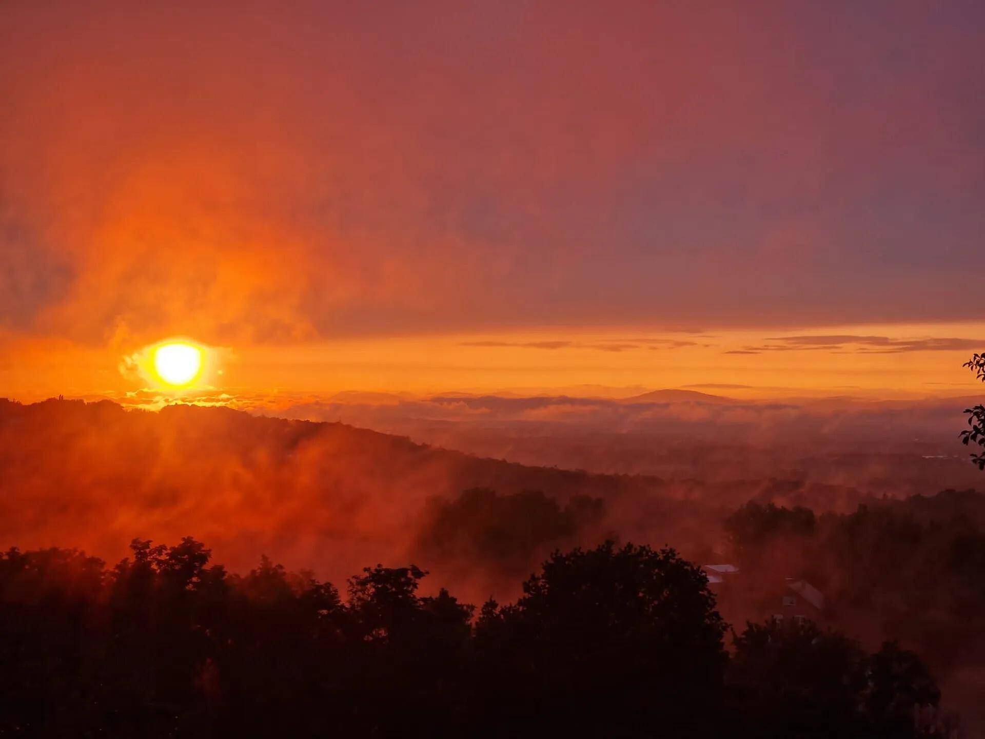 Spektakulärer Sonnenuntergang über einer nebligen Hügellandschaft mit warmen Farben.