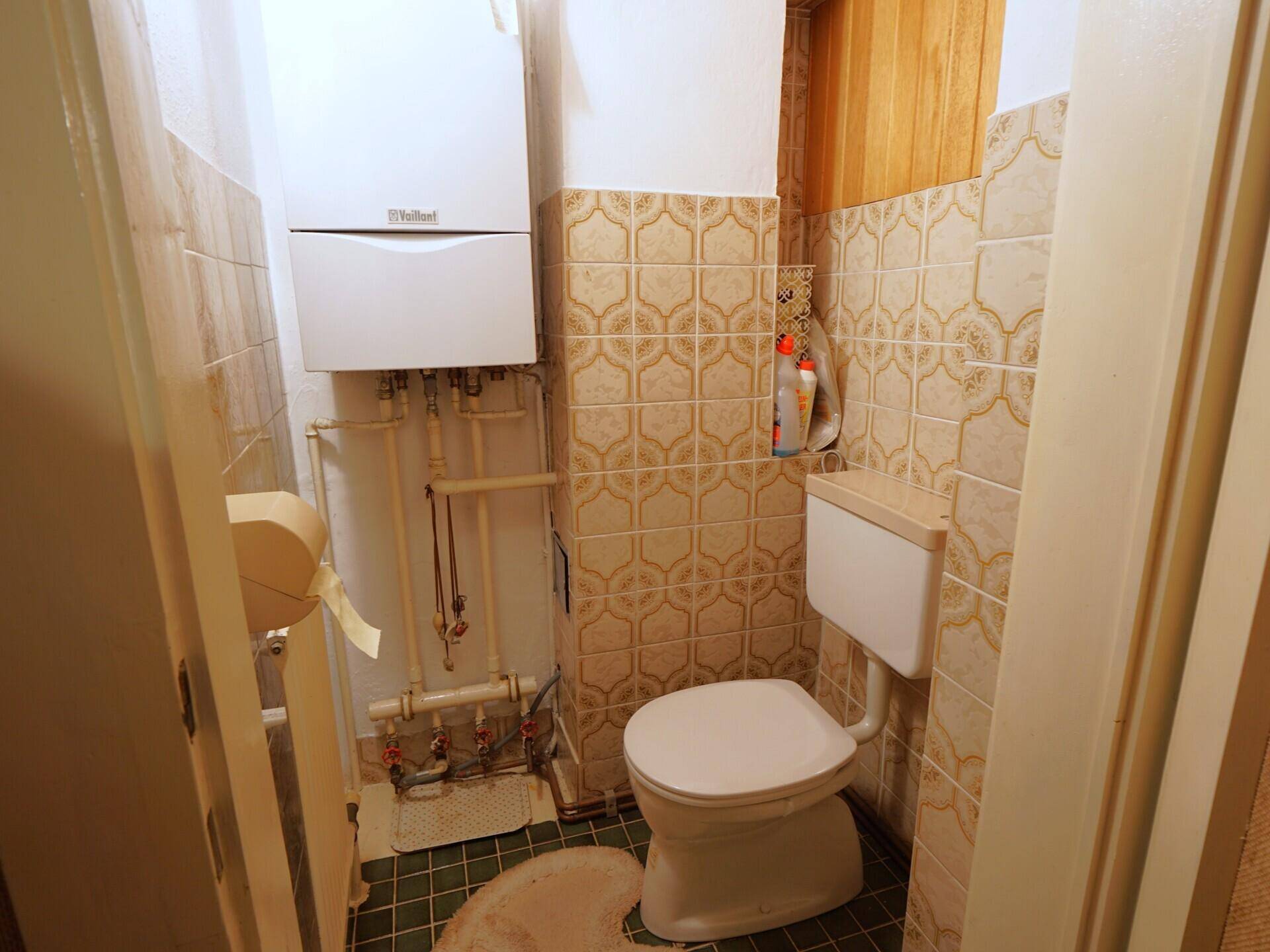 Separate Toilette mit Gastherme und Fliesen.