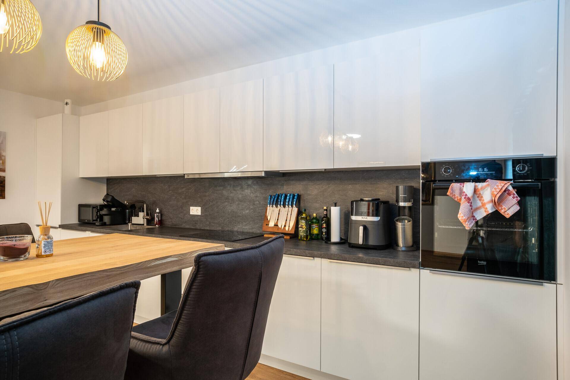 Moderne Einbauküche mit weißen Hochglanzfronten, integriertem Backofen und Bartresen.