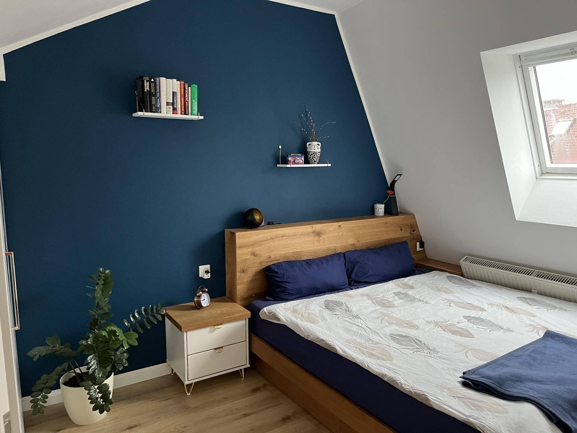 Modernes Schlafzimmer im Dachgeschoss mit blauer Akzentwand und Holzbett.