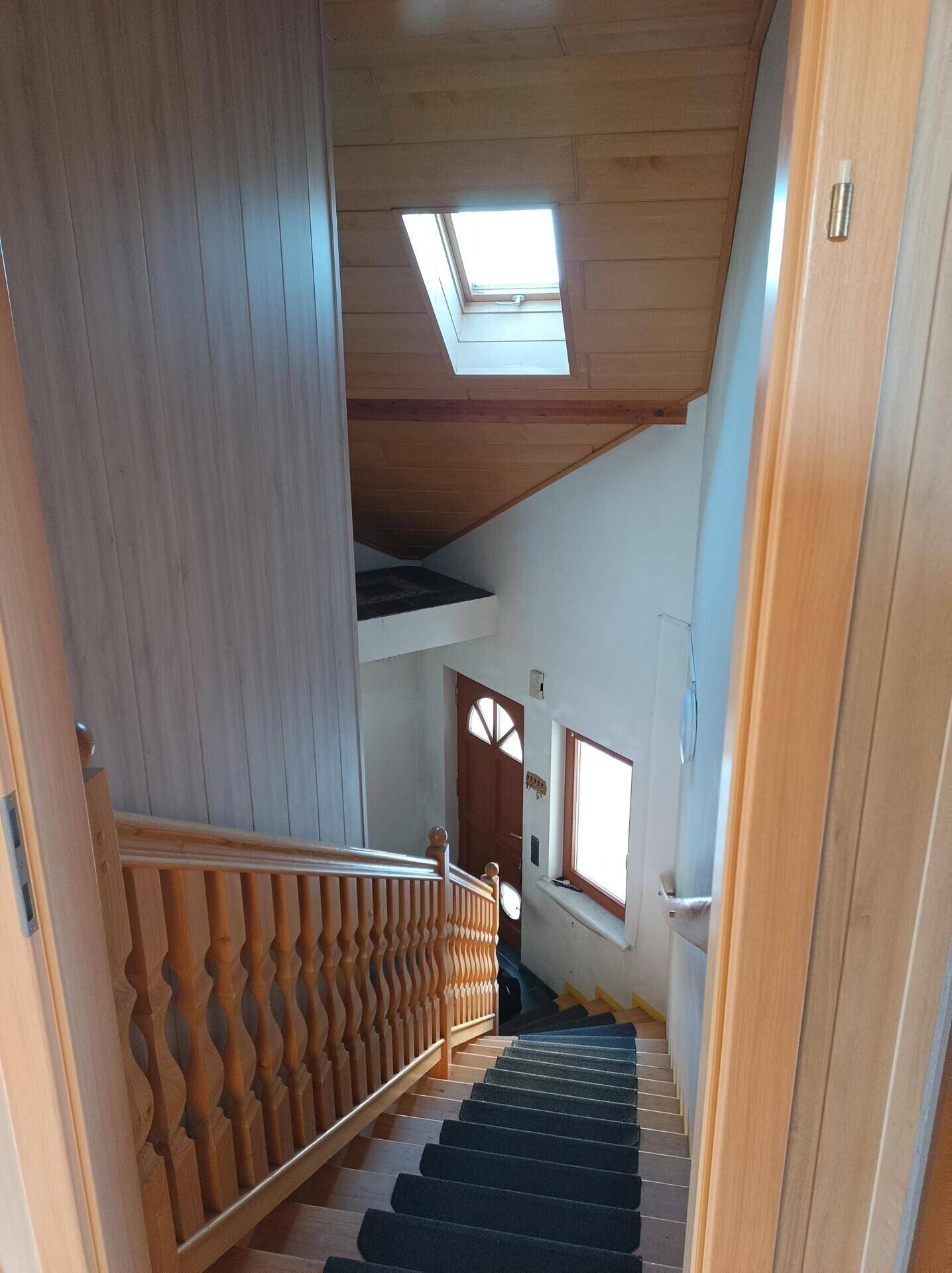 Holztreppe mit Teppichstufen und Holzgeländer, führt zu den oberen Etagen.
