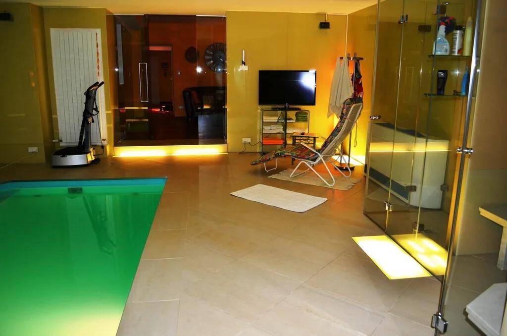 Innenpoolbereich mit Liegestuhl, Fernseher und angrenzenden Duschkabinen.