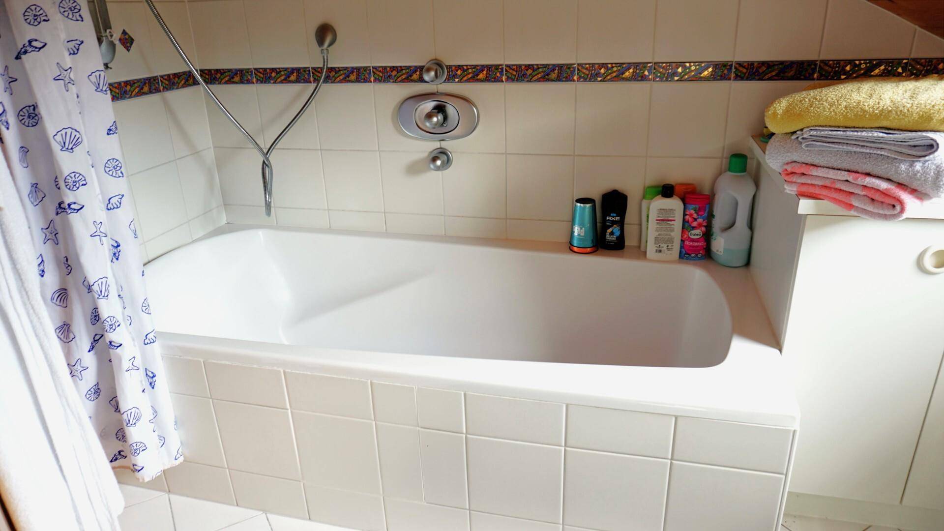 Badewanne in einem gefliesten Badezimmer mit Duschvorhang und Pflegeprodukten.
