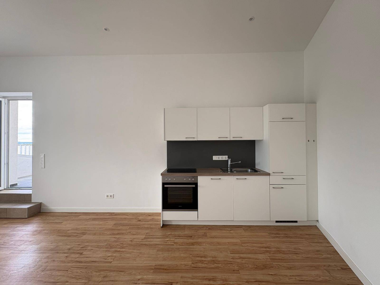 Moderne Küchenzeile mit weißen Schränken, Spüle und integriertem Backofen in hellem Wohnraum.