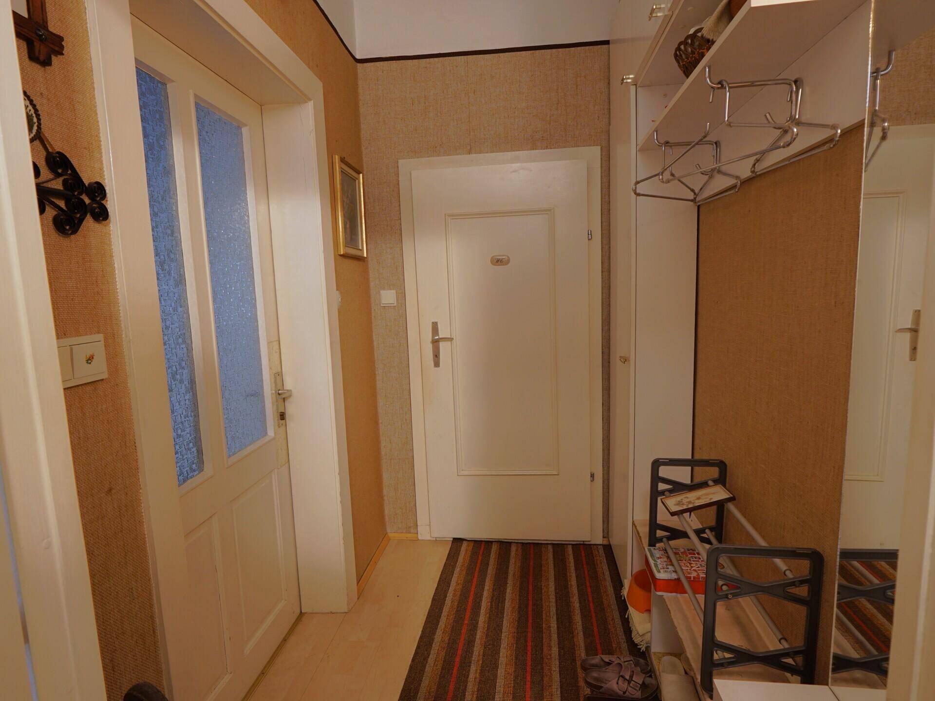 Flur mit Garderobe, Spiegel und gemusterter Tapete.