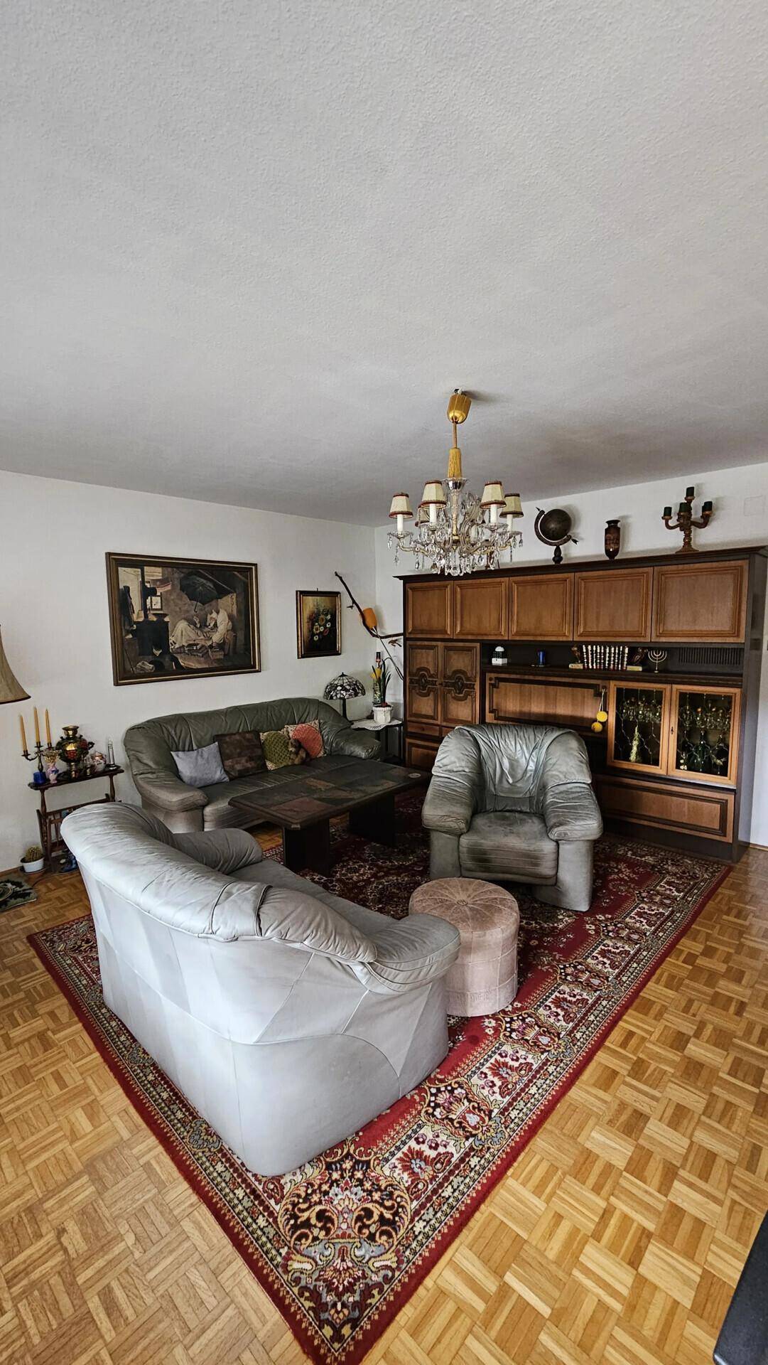 Wohnzimmer mit Ledersitzgruppe, Teppich und großem Holzschrank, klassisch eingerichtet.