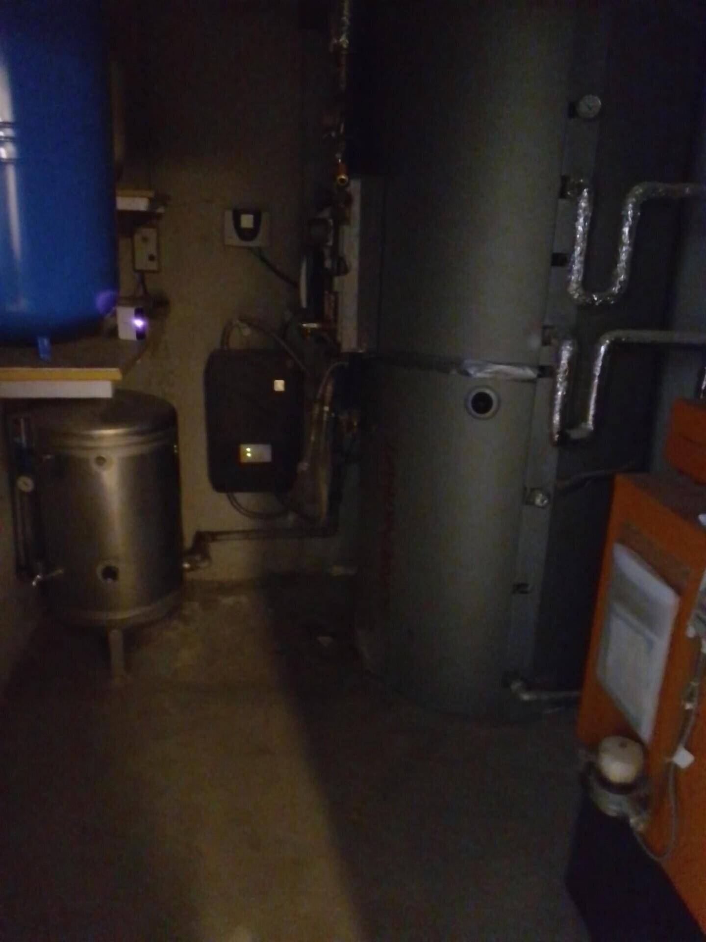 Dunkler Heizungsraum mit großen Tanks und sichtbaren Rohren für die Haustechnik.