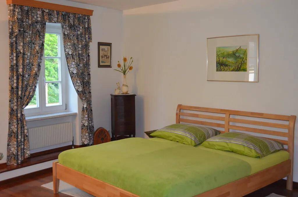 Gemütliches Schlafzimmer mit Holzbett, grüner Bettwäsche und Fenster mit Blick ins Grüne.