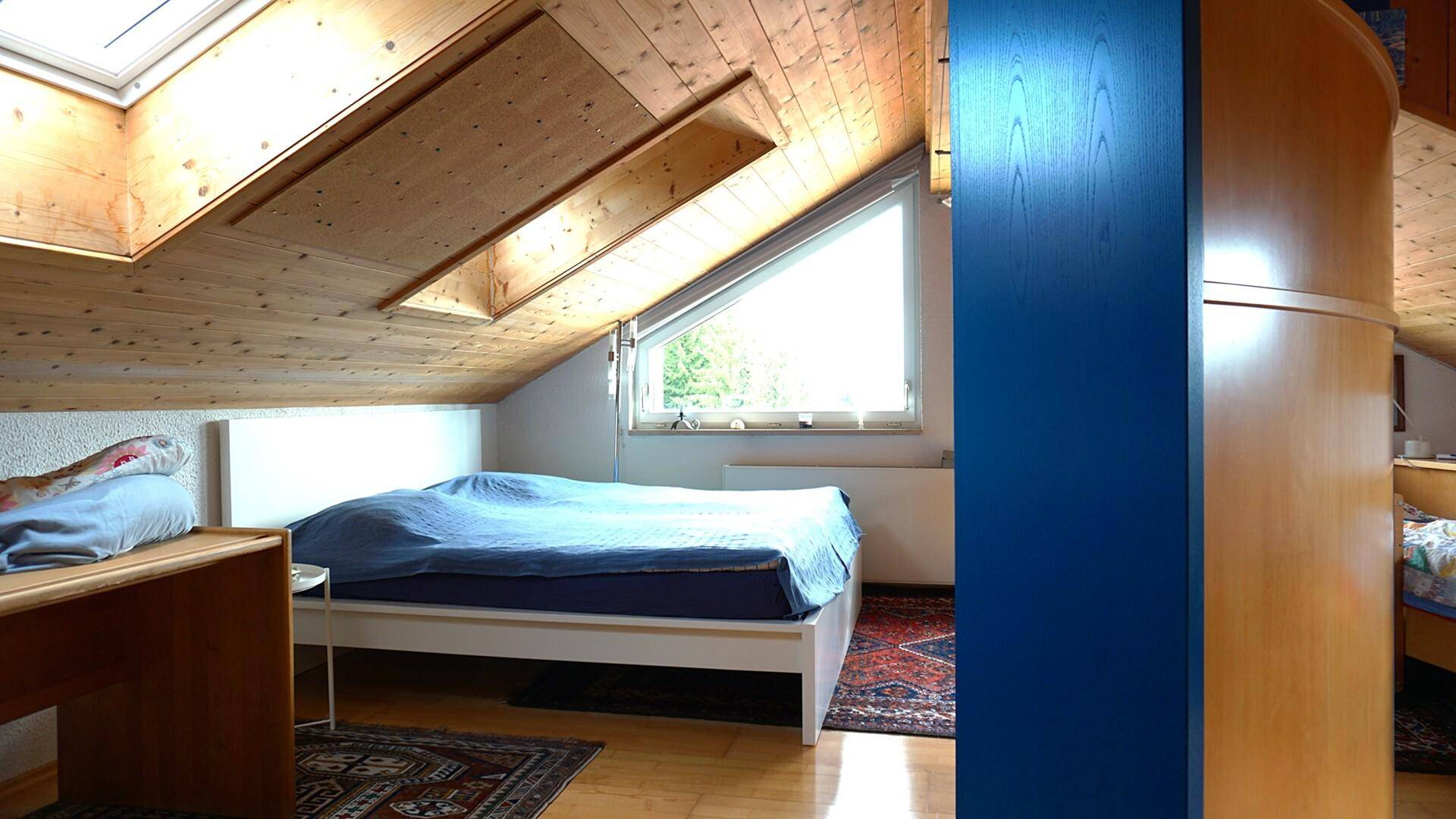 Schlafzimmer im Dachgeschoss mit Holztäfelung, Dachschrägen und Dachfenstern.