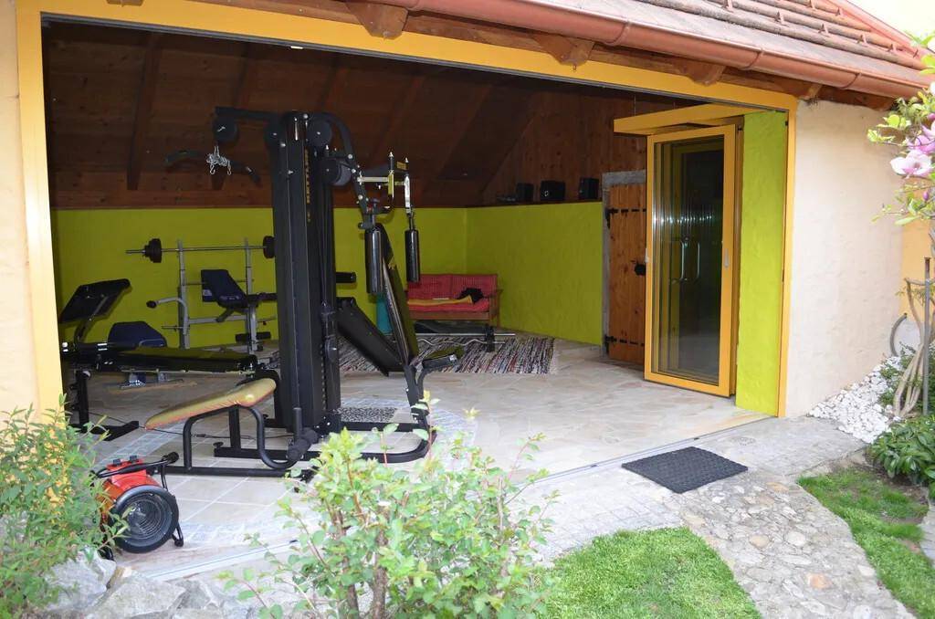 Außenansicht des Fitnessraums mit offenem Zugang zum Garten und Steinplatten.