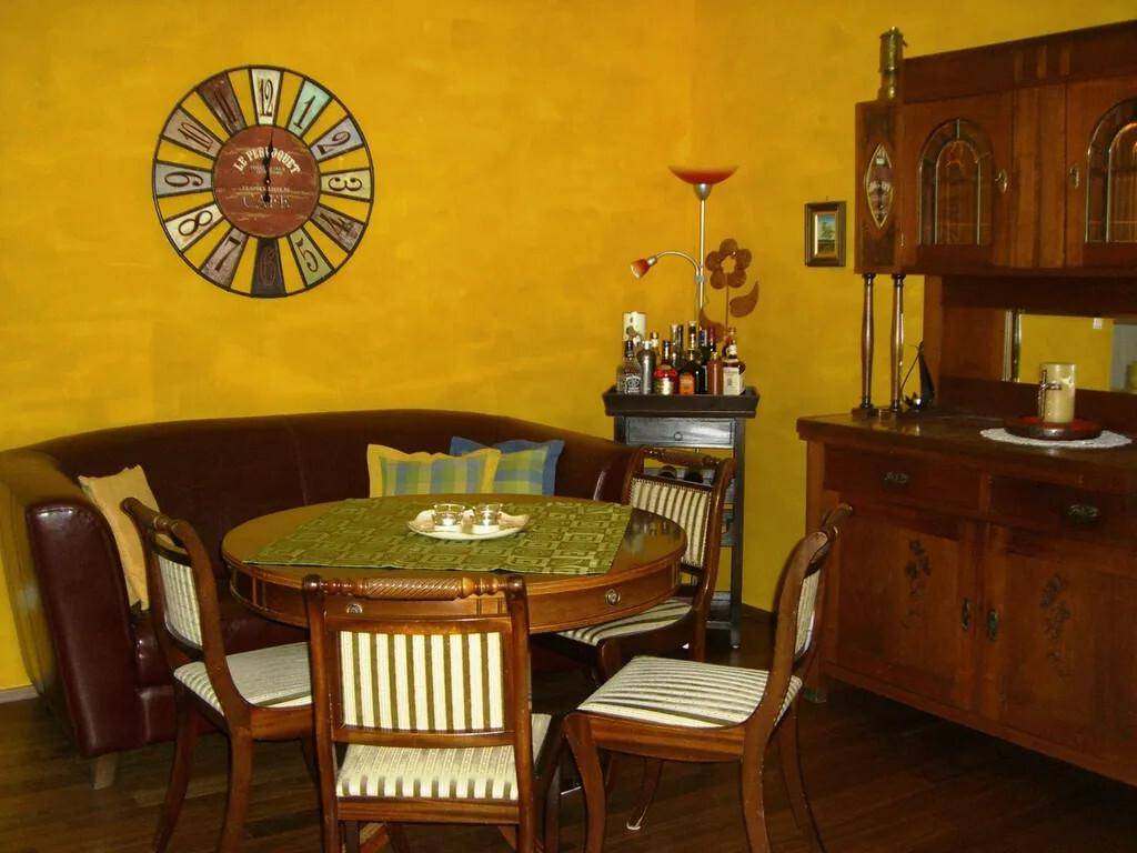 Essbereich mit runden Holztisch, traditionellen Möbeln und großer Wanduhr.