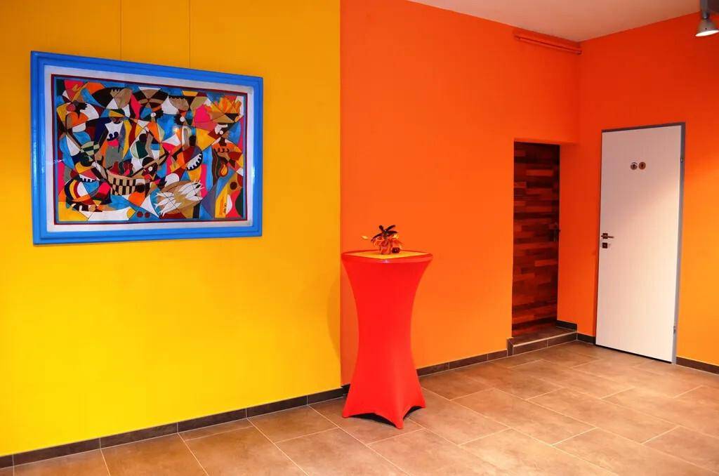 Heller Flur mit leuchtend gelben und orangen Wänden, modernem Kunstwerk und Steinfliesenboden.