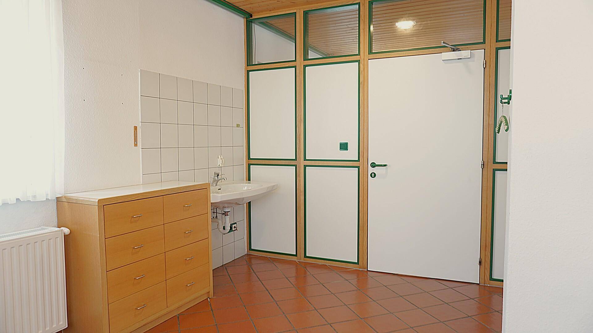 Praktischer Raum mit Waschbecken, Holzkommode und Fliesenboden.