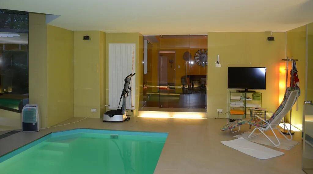 Geräumiger Innenpoolbereich mit Liegestuhl, Fitnessgerät und Blick durch Glastüren.