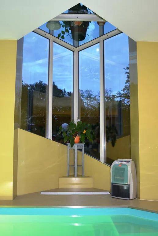 Innenpoolbereich mit großer Glasfront, gelben Wänden und Blick ins Freie.