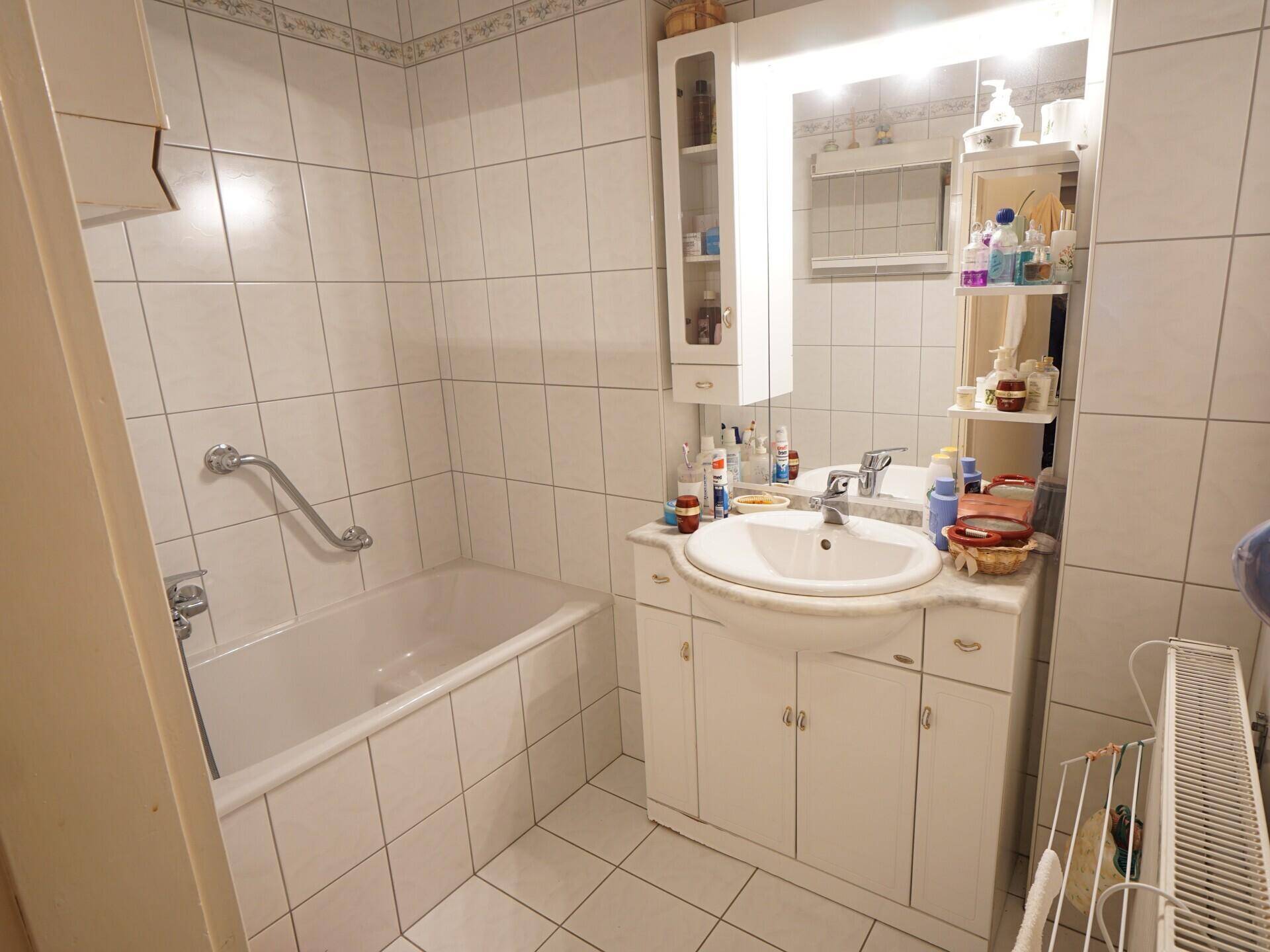 Badezimmer mit Badewanne, Einzelwaschbecken und weißen Fliesen.