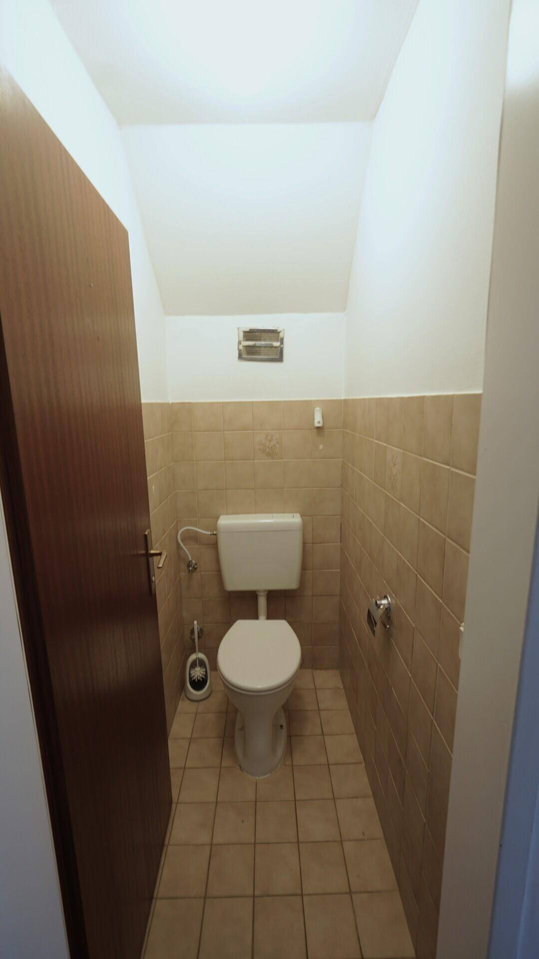 Separates WC mit Toilette und beigefarbenen Wand- und Bodenfliesen.