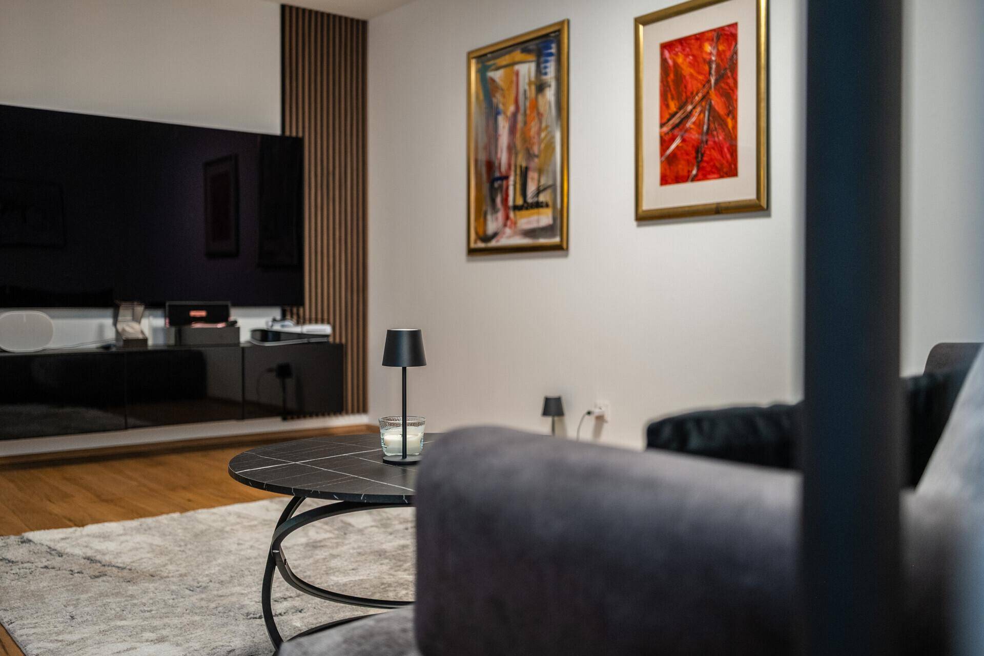 Detailansicht des Wohnzimmers mit moderner Couch, Couchtisch und farbenfrohen Kunstwerken an der Wand.