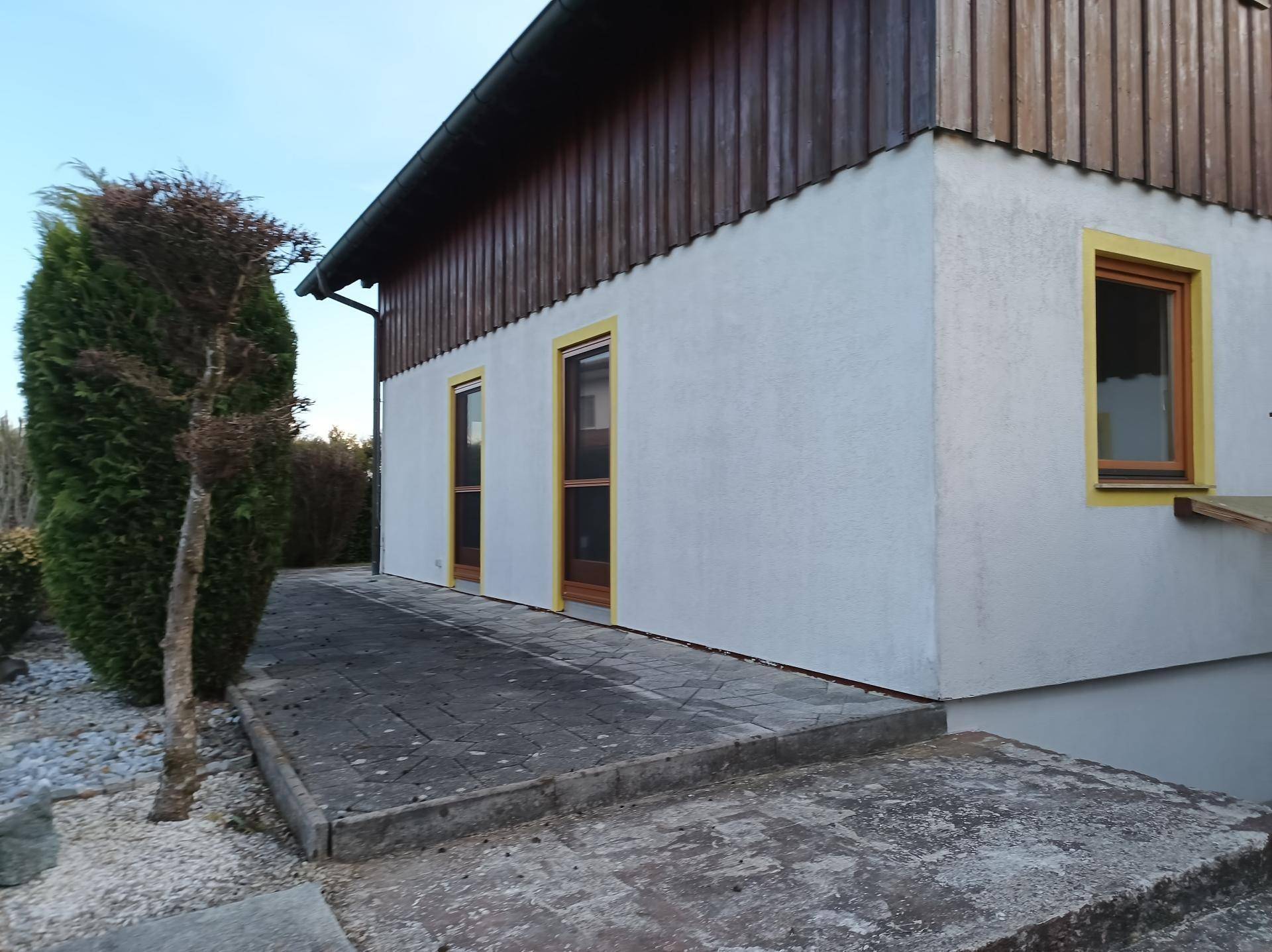 Seitenansicht des Hauses mit Holzelementen und gepflastertem Bereich.