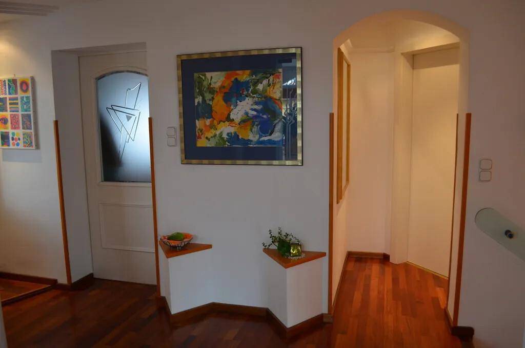Heller Flur mit Holzboden, Kunstwerken und einer Tür mit Milchglas.
