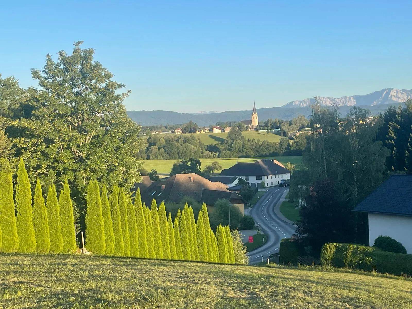 Sommerlicher Ausblick auf ein idyllisches Dorf mit Kirche und Bergpanorama im Hintergrund.