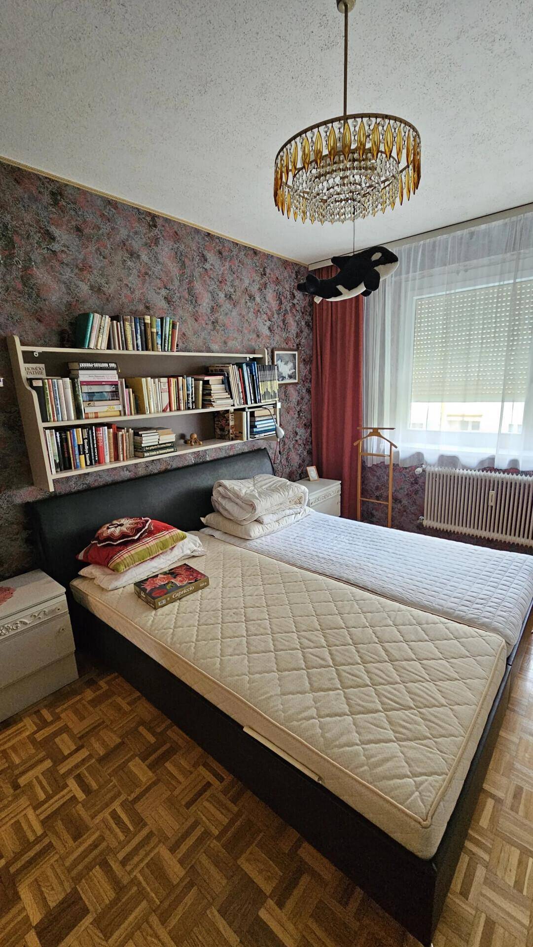 Schlafzimmer mit zwei Einzelbetten, Bücherregal über dem Bett und einem Kronleuchter.