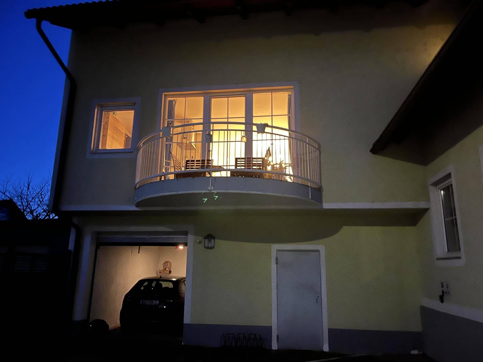 Außenansicht des Hauses bei Nacht mit beleuchtetem Balkon und Garage.