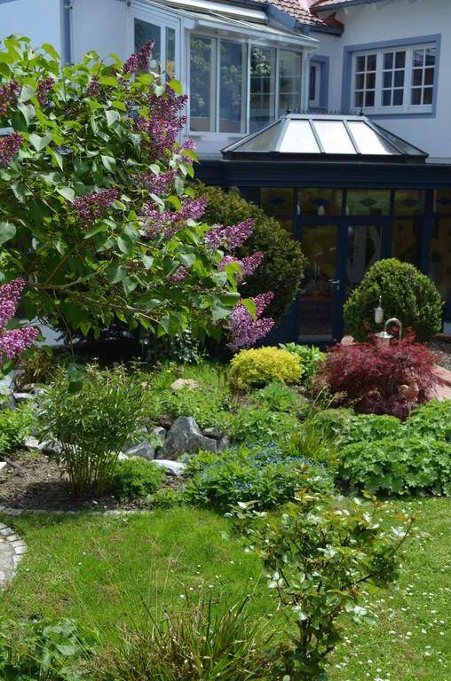 Blühender Garten mit Fliederbüschen, Rasenfläche und einem Wintergarten am Wohnhaus.