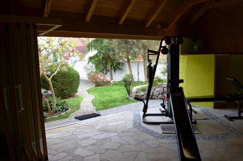 Blick vom Fitnessraum in den gepflegten Garten mit Steinweg und Grünflächen.