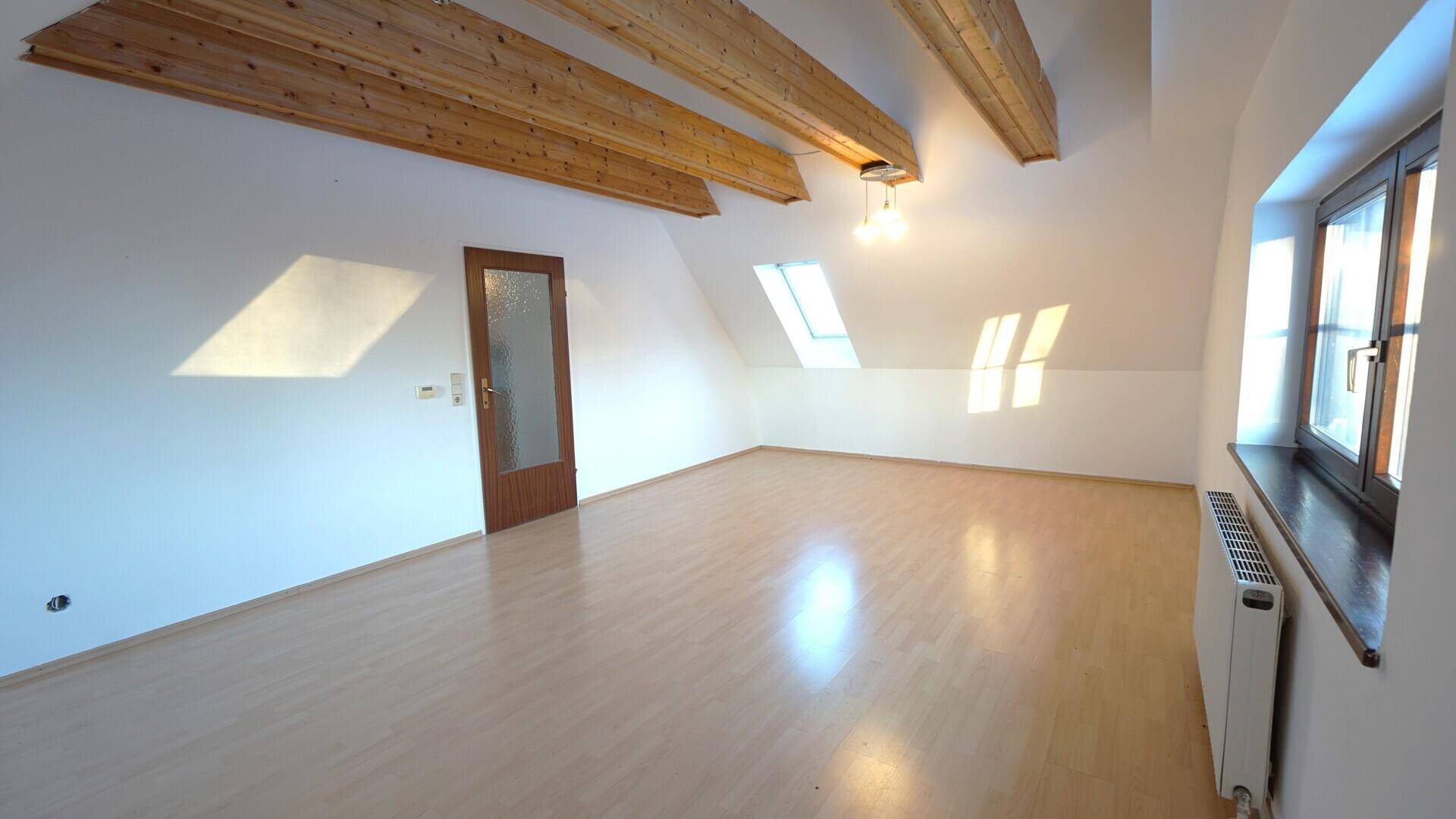 Heller Wohnraum im Dachgeschoss mit sichtbaren Holzbalken, Dachschrägen und Laminatboden.