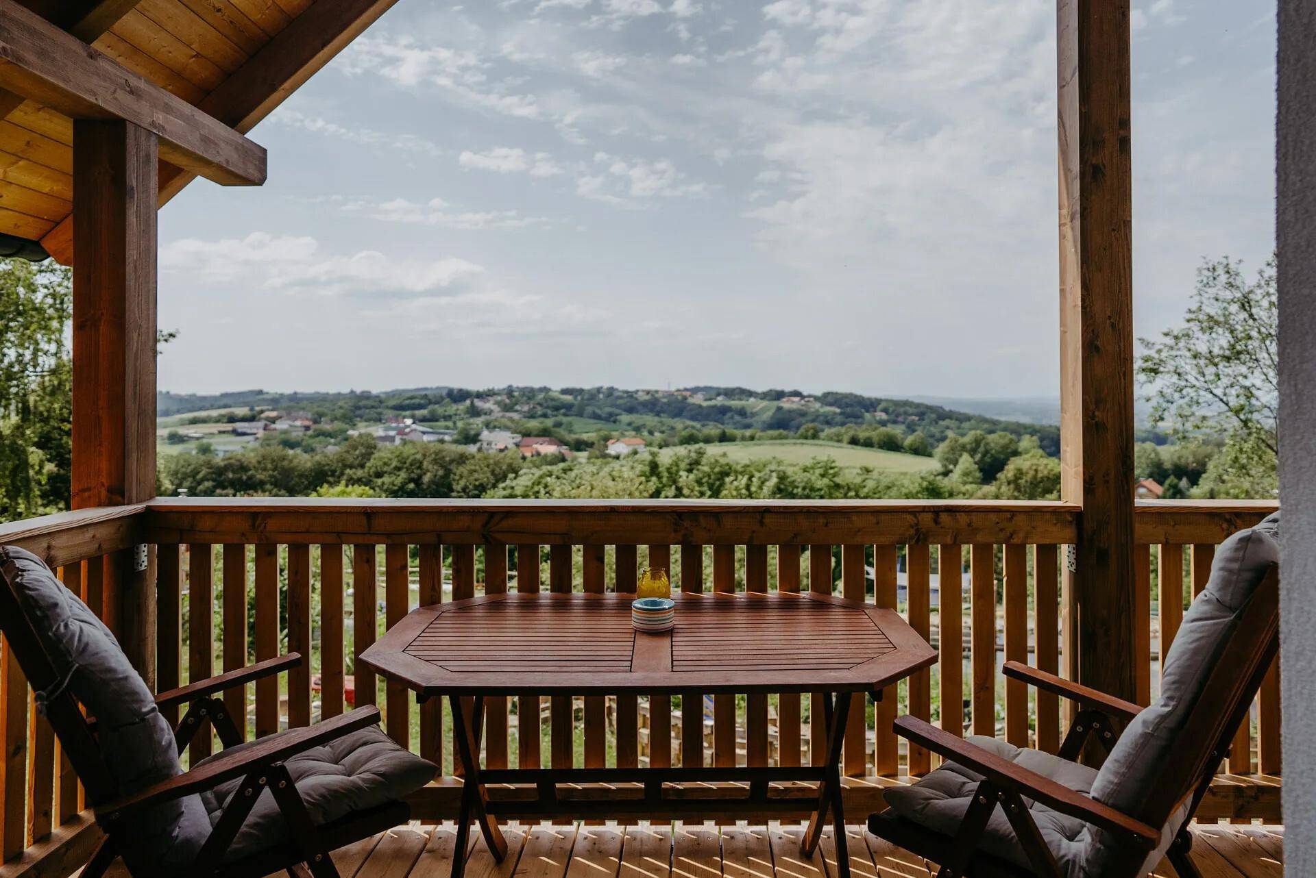Überdachter Balkon mit Holztisch und Stühlen, bietet einen weiten Blick über die Landschaft.