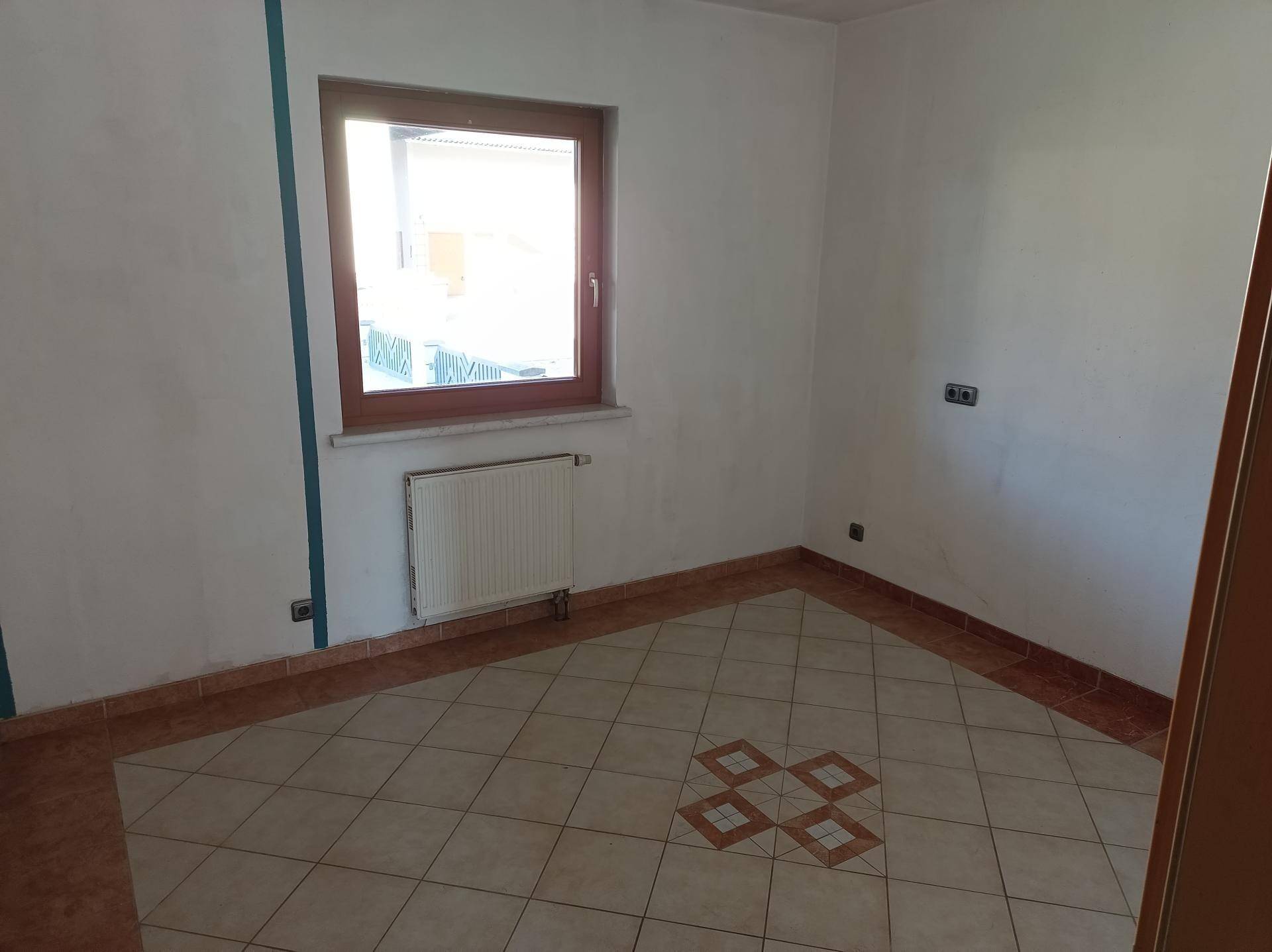 Kleiner Raum mit Fliesenboden, Heizkörper und Fenster, ideal als Abstellraum.