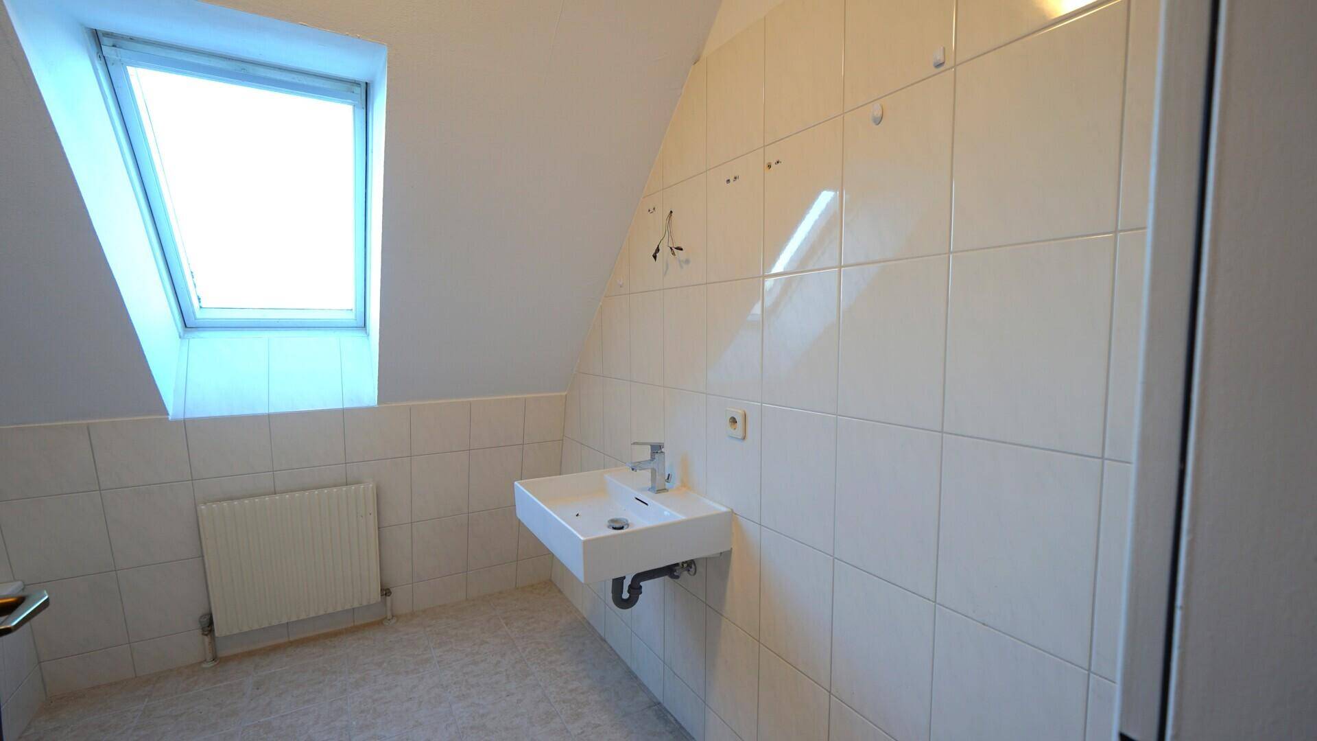 Helles Badezimmer im Dachgeschoss mit Waschbecken, weißen Fliesen und Dachfenster.