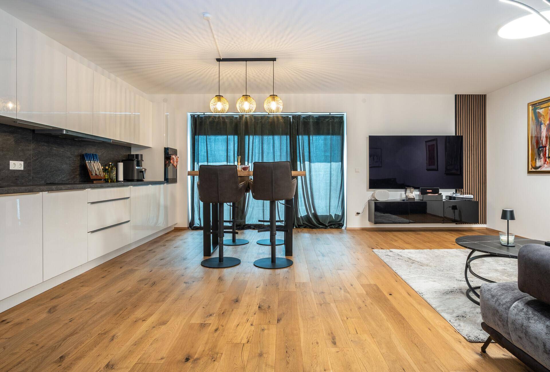 Heller offener Wohnbereich mit integrierter Küche, Bartresen und Zugang zum Balkon.