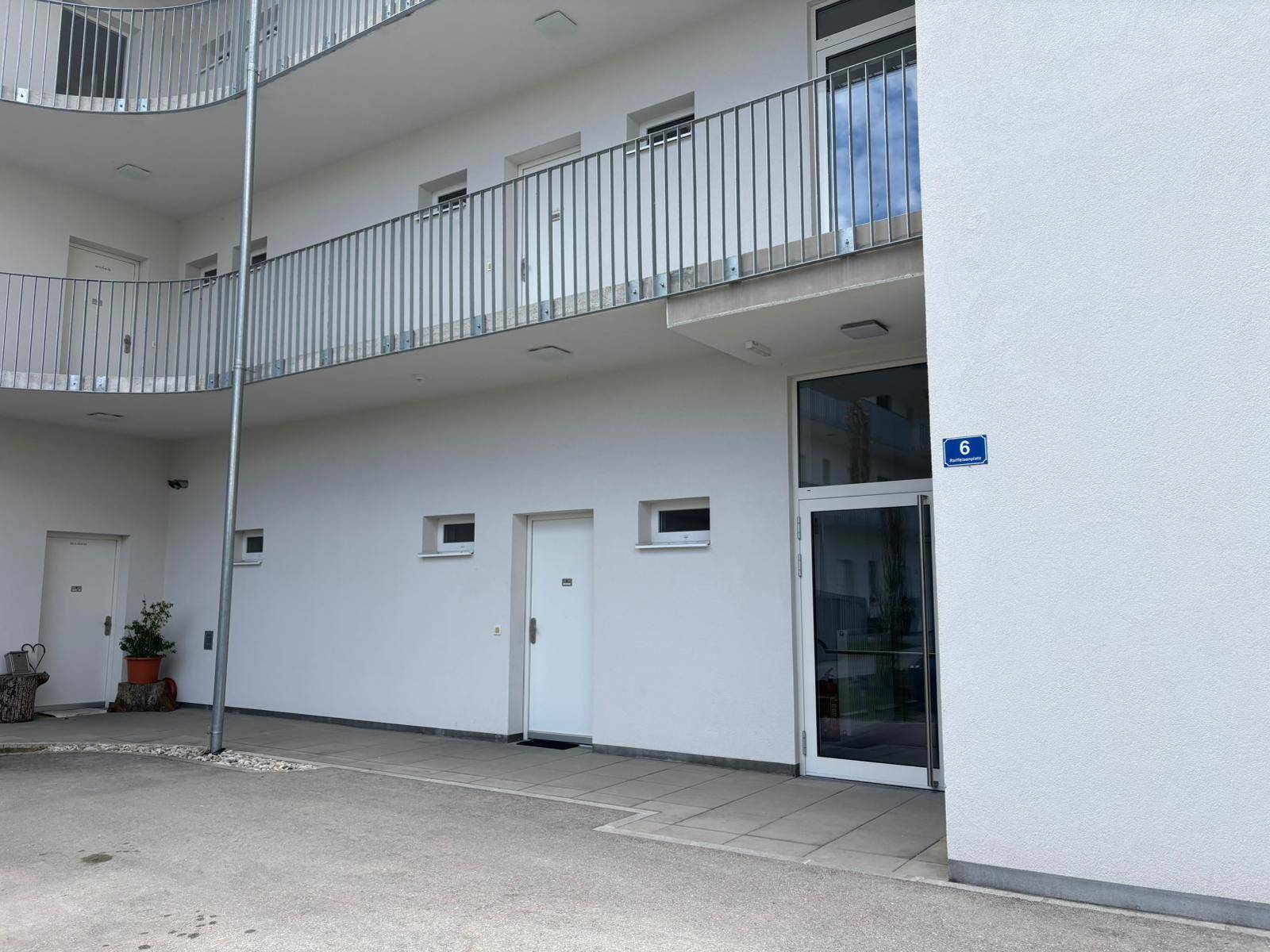Eingangsbereich eines modernen Apartmentgebäudes mit Hausnummer und geschwungenen Balkonen.