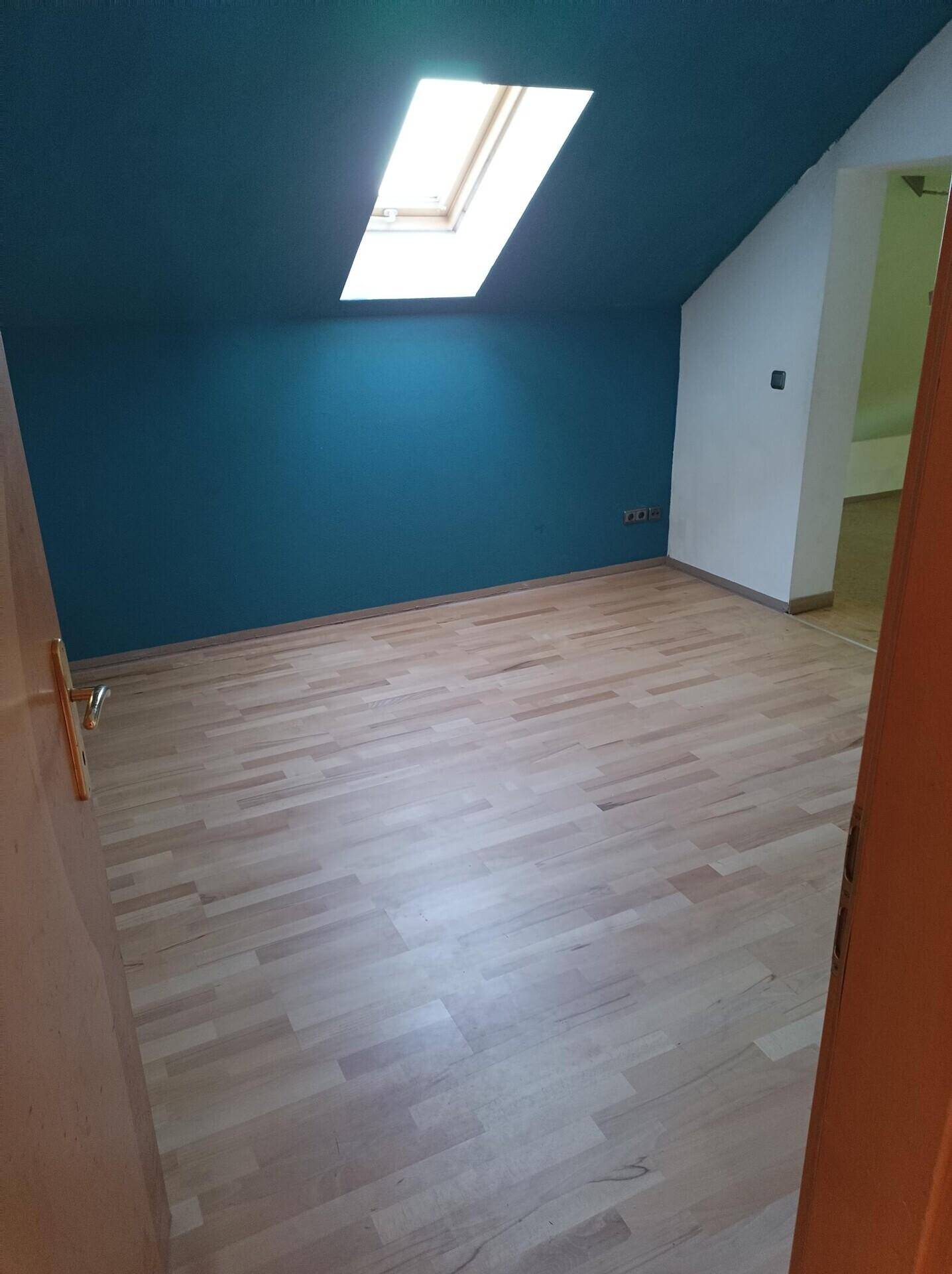 Geräumiges Schlafzimmer im Dachgeschoss mit Holzboden, blauer Wand und Dachfenster.