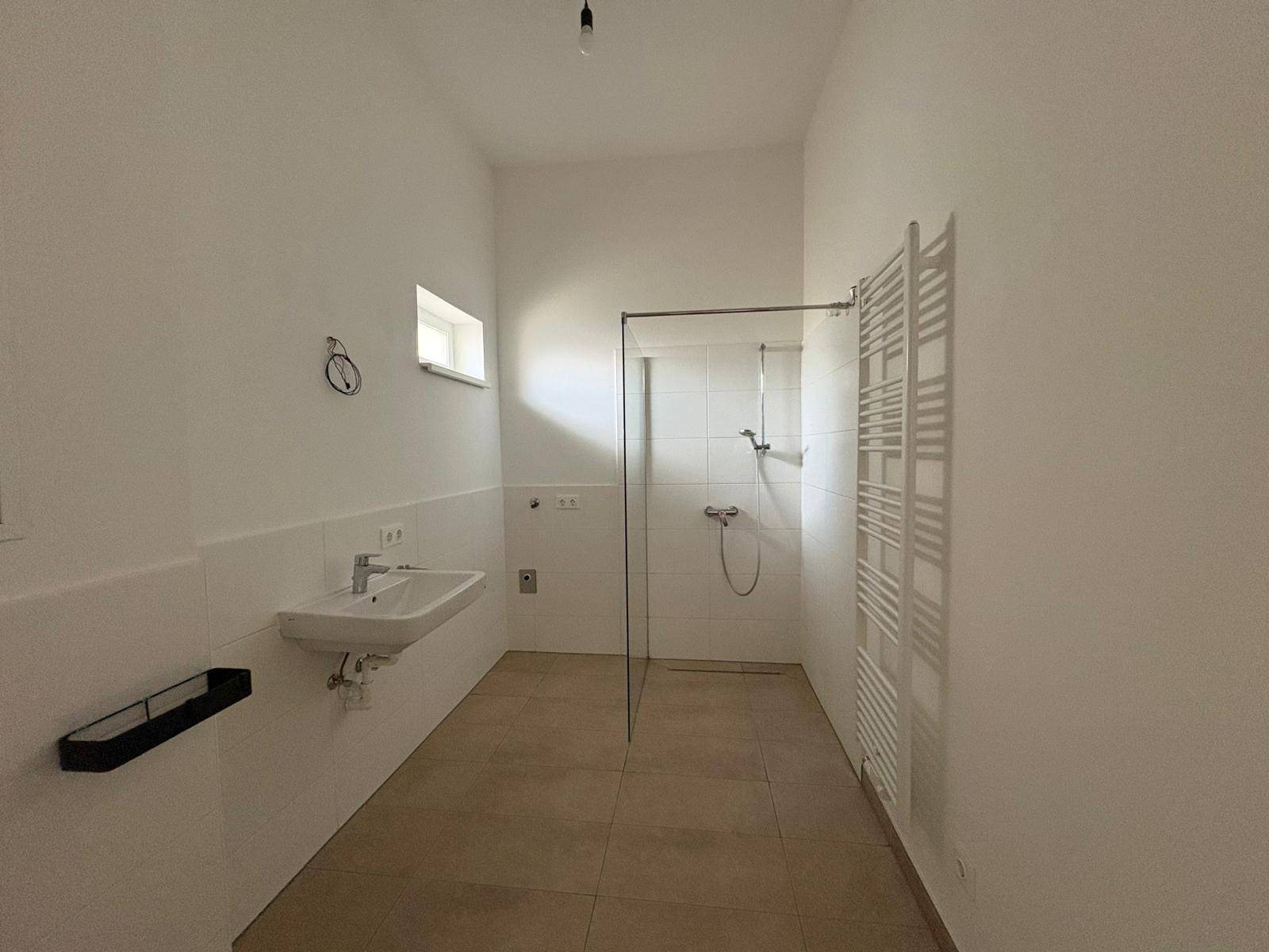Modernes Badezimmer mit ebenerdiger Dusche, Waschbecken, beheiztem Handtuchhalter und Fenster.