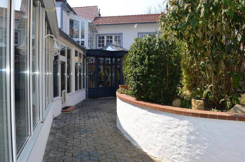 Gepflasterter Weg zwischen dem Wintergarten und einem gepflegten Gartenbereich.