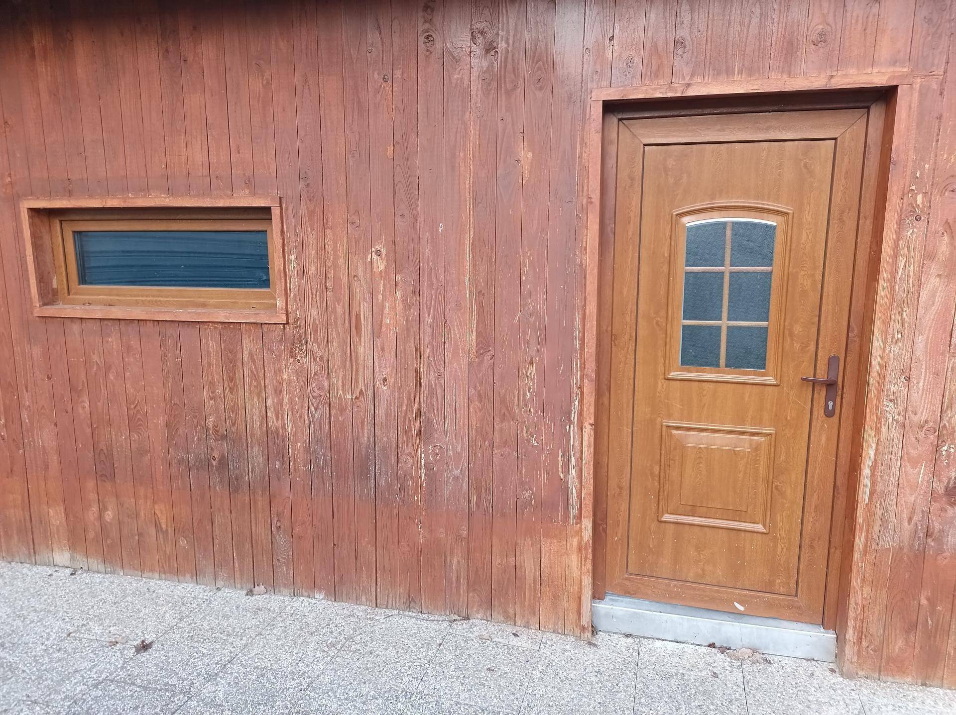 Holzwandfassade mit einer braunen Eingangstür und einem kleinen Fenster.