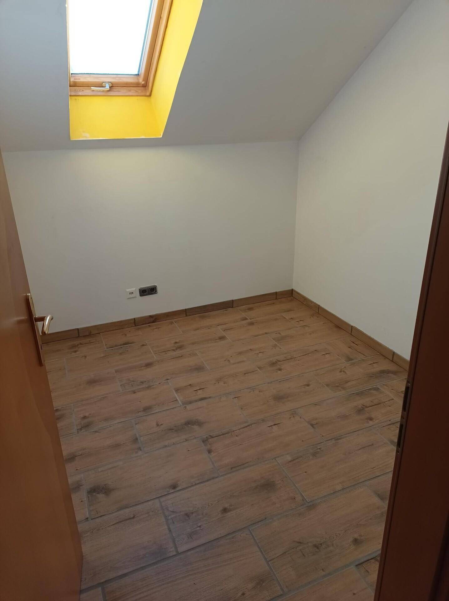Helles Zimmer im Dachgeschoss mit Holzboden und Dachfenster für natürliches Licht.